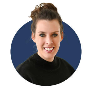 A smiling woman with brown hair styled in a bun is wearing a black sweater. The background is a solid dark blue circle.