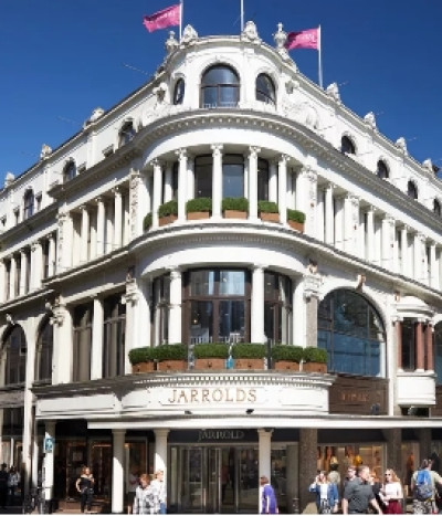 An elegant, historic building with ornate architectural details featuring multiple stories, large windows, and decorative columns. The top is adorned with flags, and the entrance displays the name 