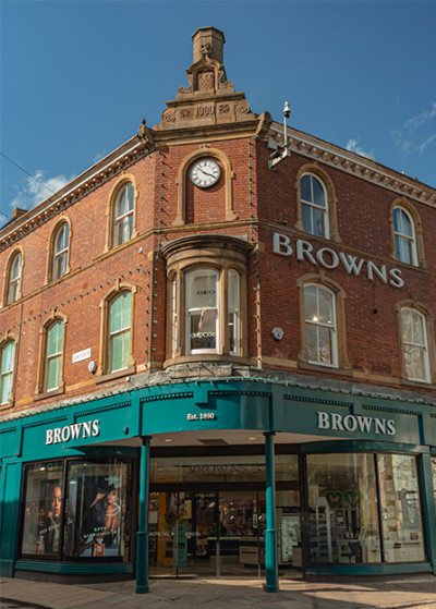 Victorian-style corner building with brick facade and large glass windows. The name 
