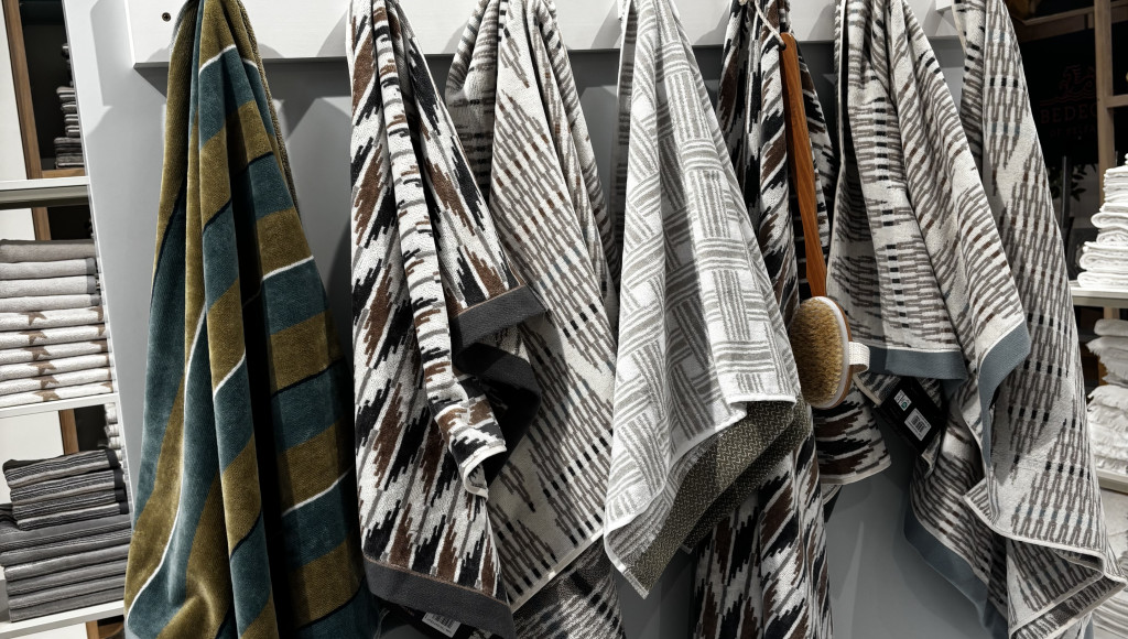 A display featuring a variety of patterned towels hanging on a rack. The towels showcase different designs and colors, with a sign above reading 