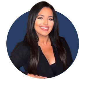 A woman with long, dark hair smiles confidently while wearing a black blazer over a black top. The background is a solid blue circle.