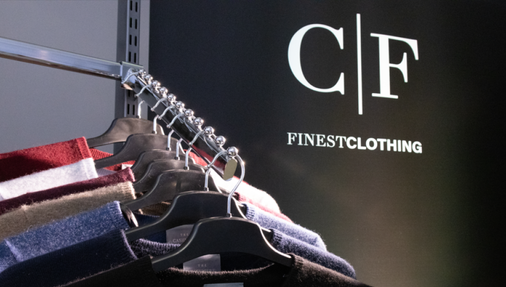 A clothing rack displaying various sweaters in different colors, with a backdrop featuring the logo 